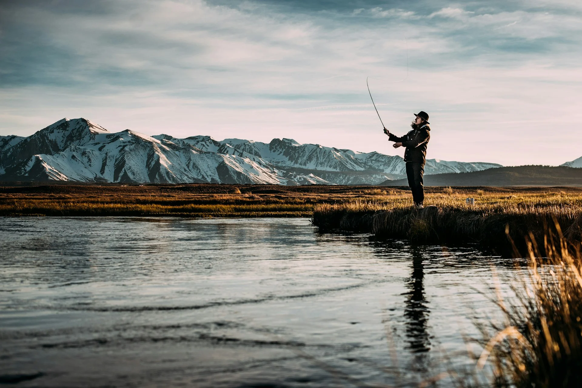 Angler fly fishing on a lake below mountains