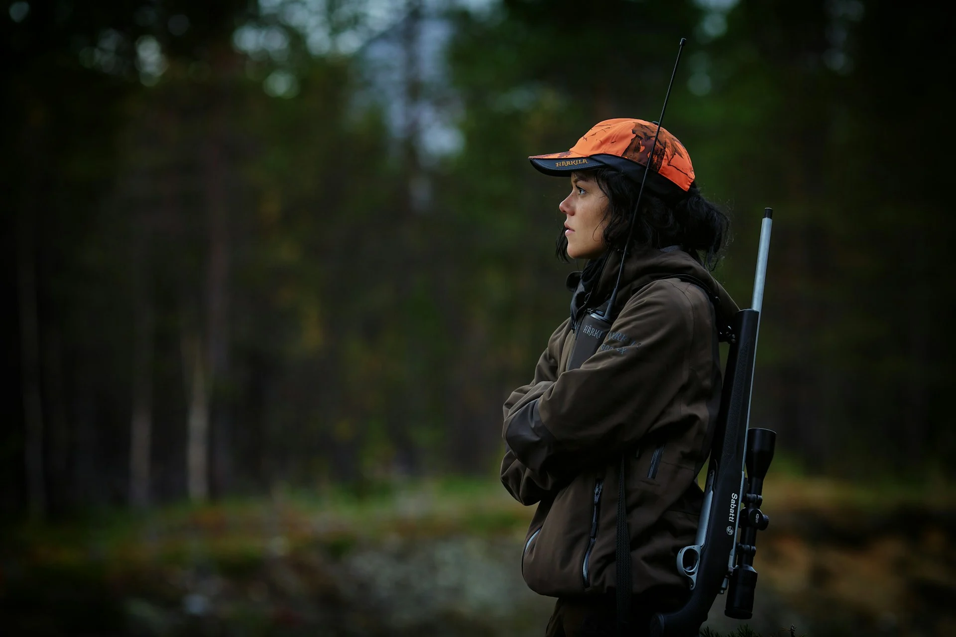 Hunter in a blaze orange cap carrying a rifle in the forest
