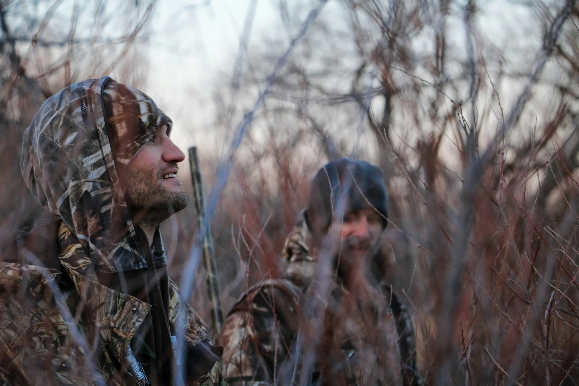 Two hunters in camouflage sitting in tall dry grass