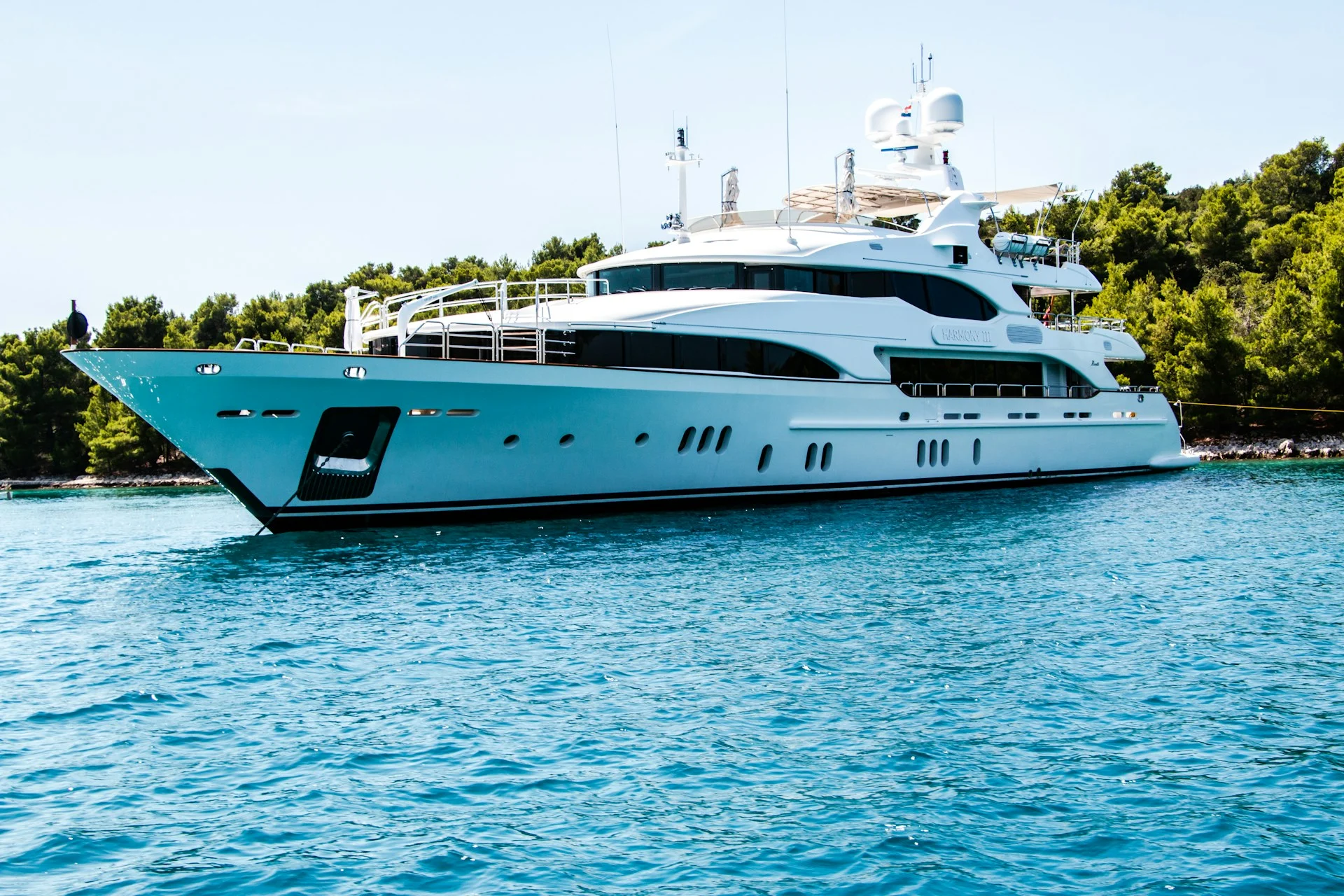 Large white yacht cruising near a wooded shore