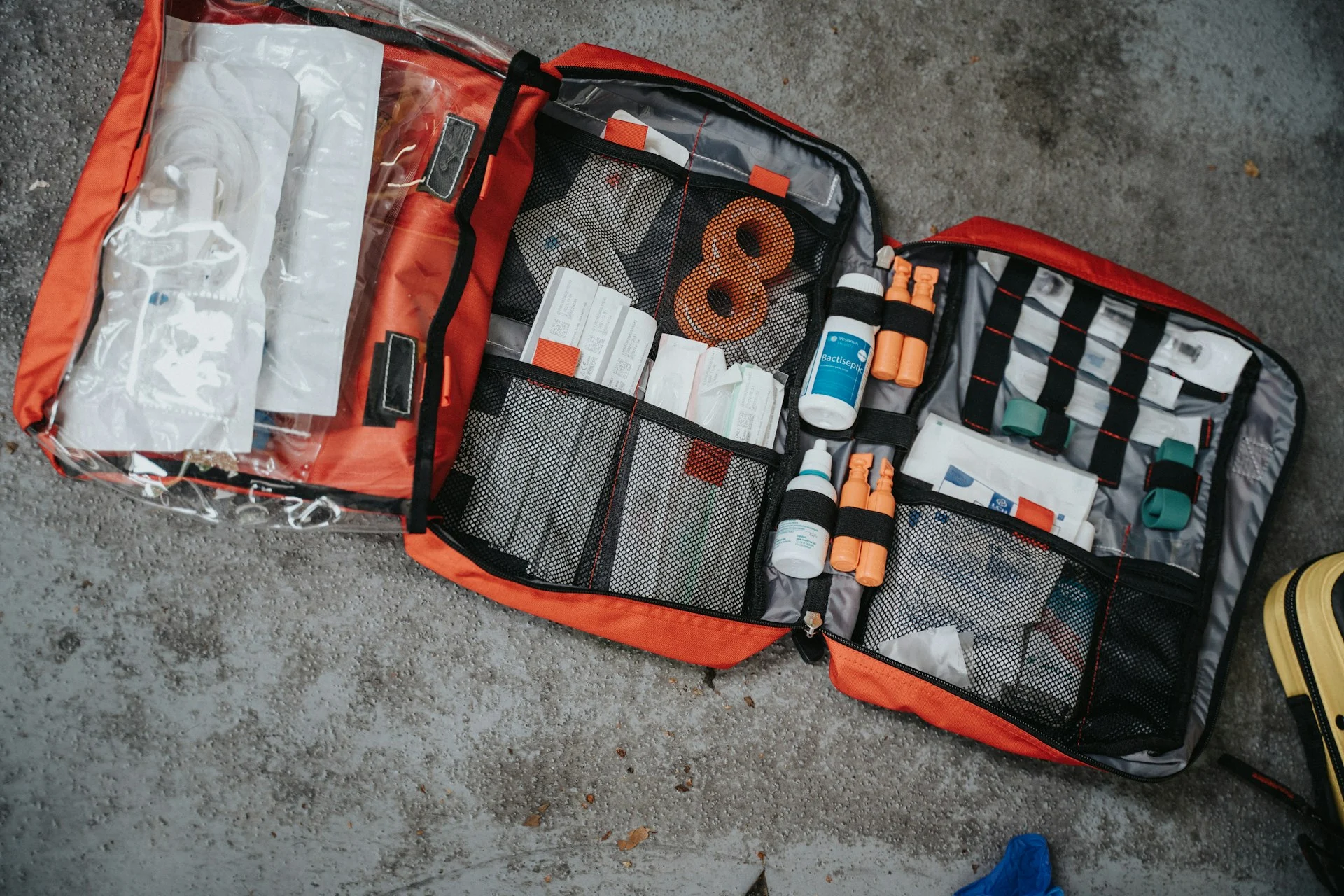 An open red medical bag filled with various supplies on a grey surface