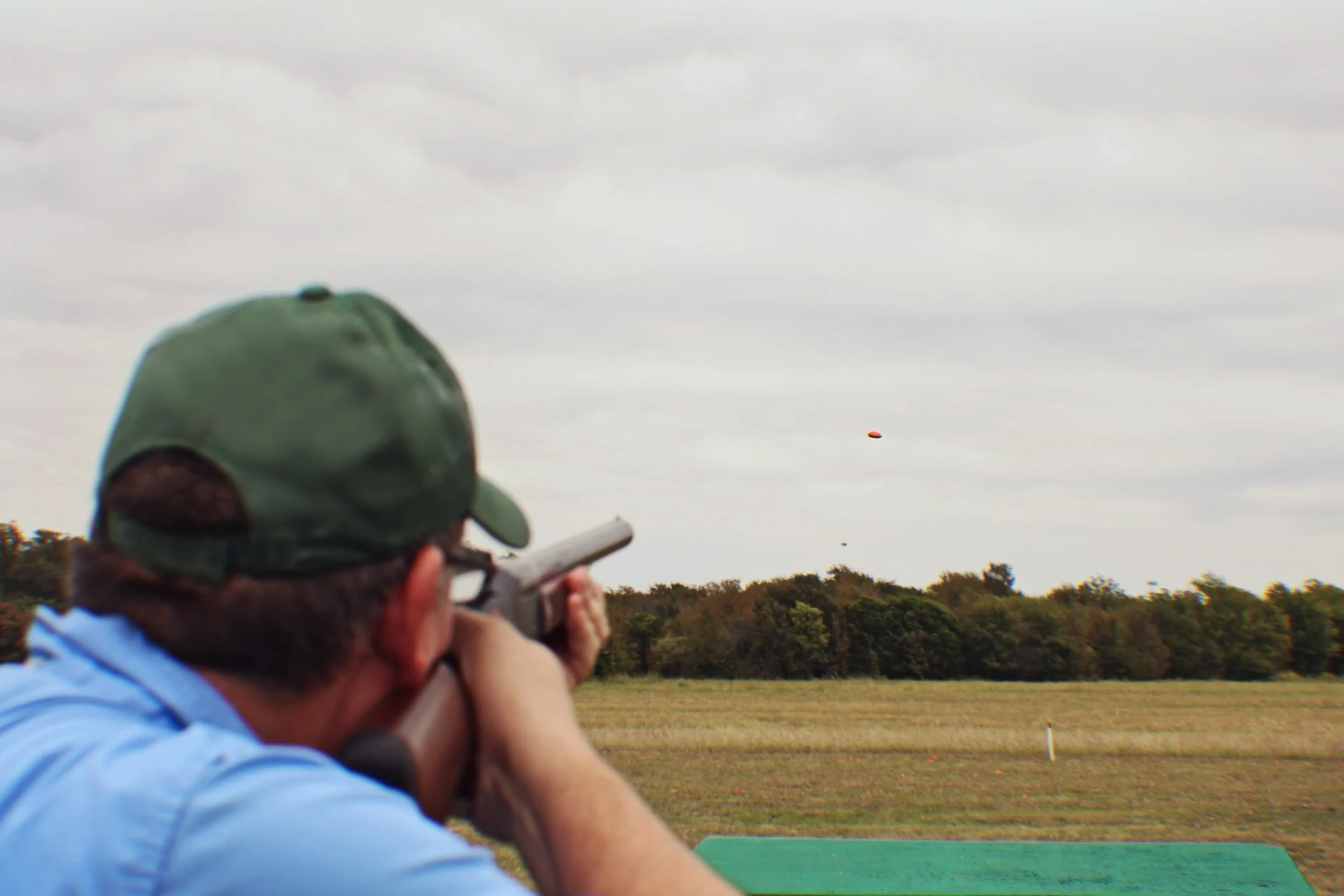 Shooter in a ball cap aiming a shotgun