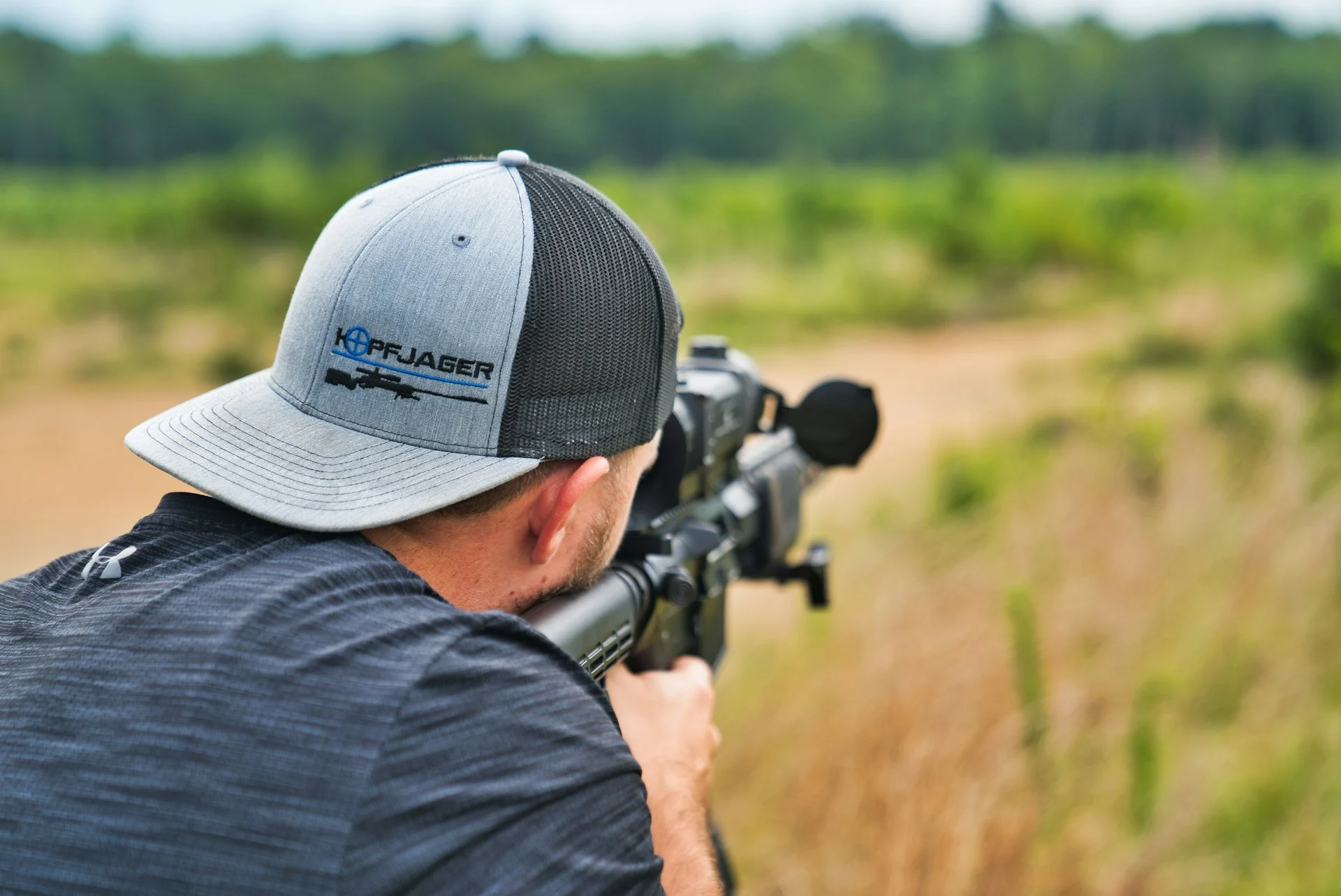 Shooter aiming a scoped rifle across an open field